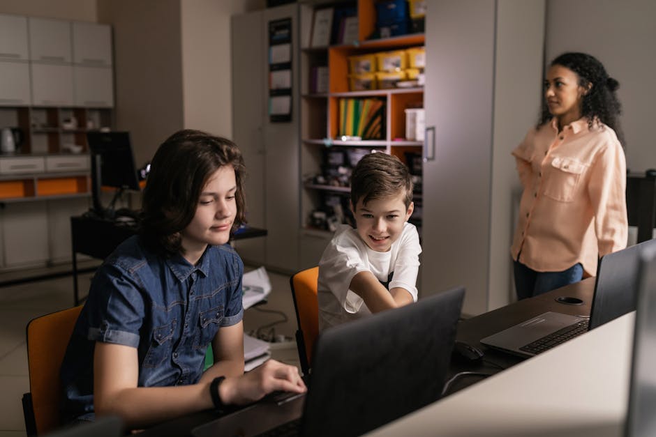 Students using laptops in a classroom setting with a teacher supervising, promoting digital education.