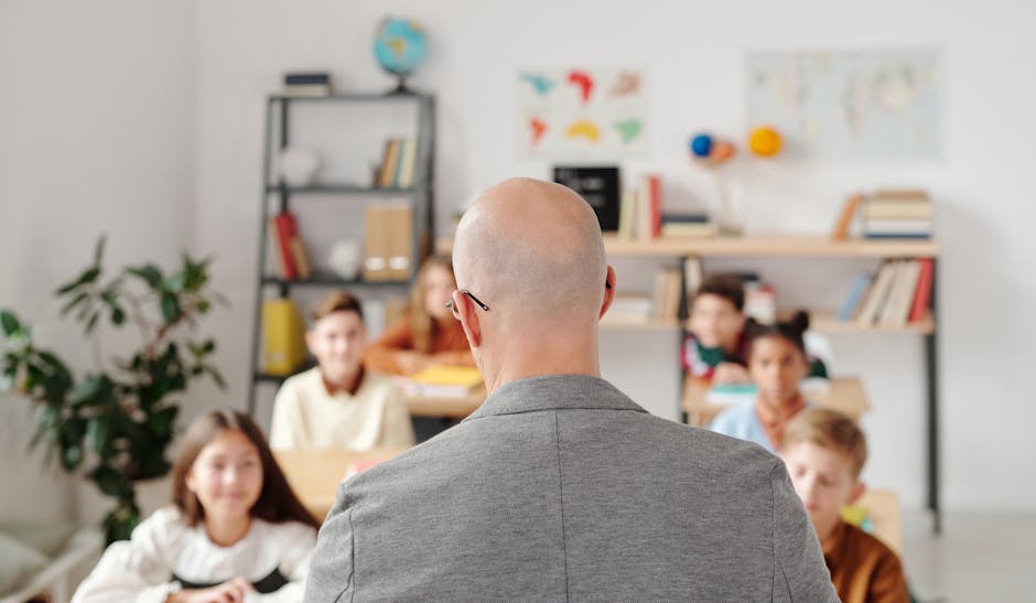 Bald teacher in a classroom engaging with attentive students sitting at desks